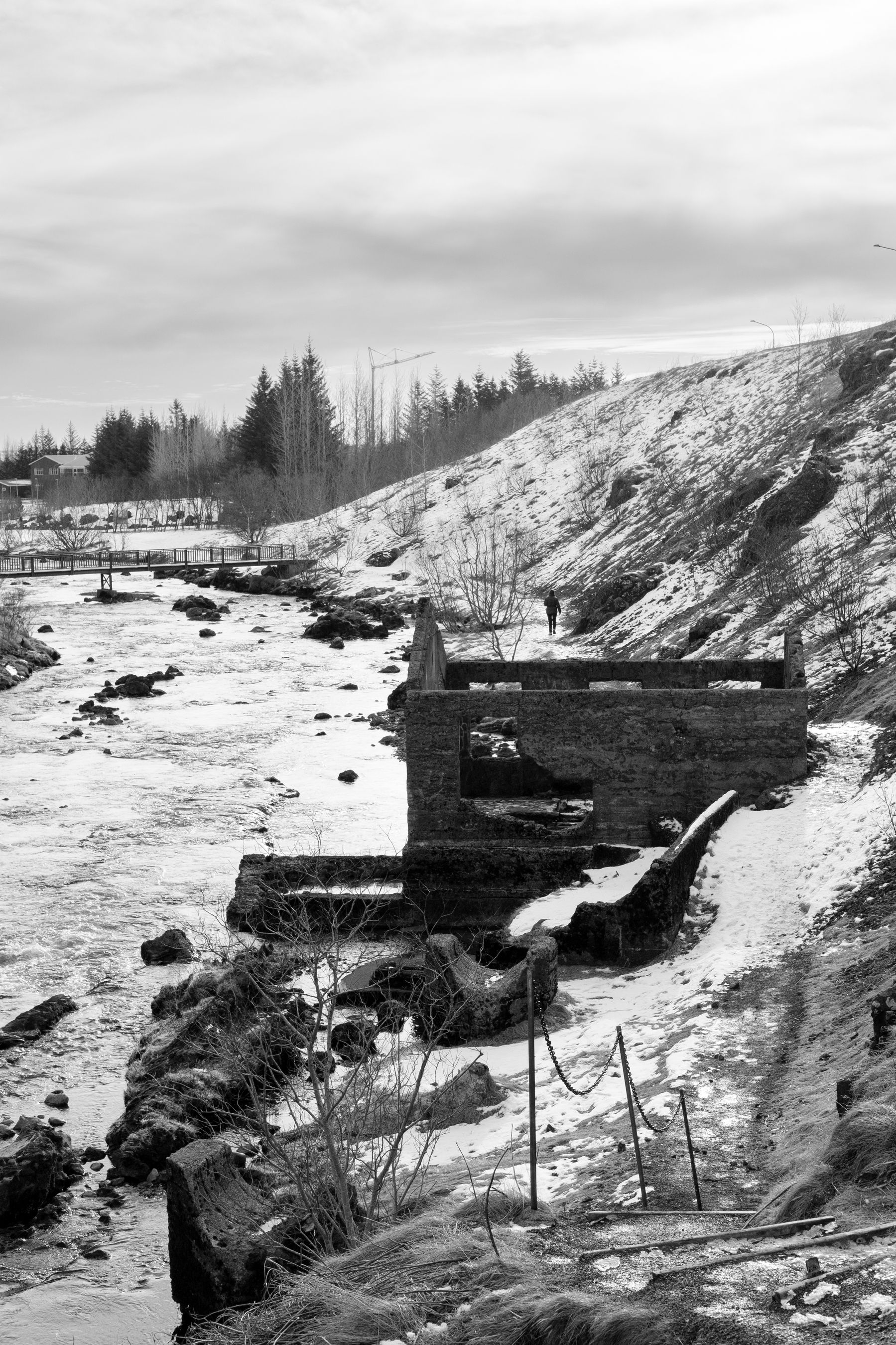 A wider view of that ruined building, the river, and the path next to it. Everything is covered with snow.