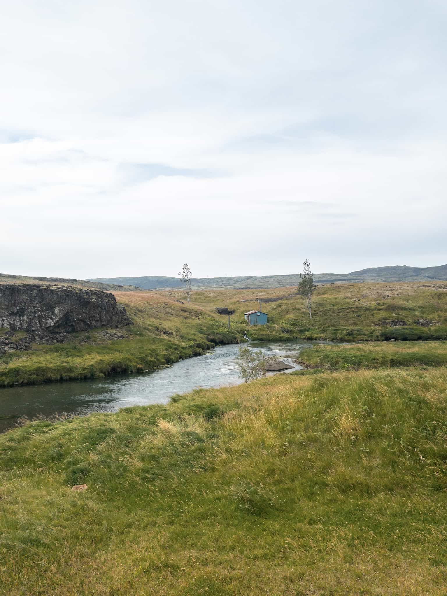 A small shed made out of rusty corrugated iron by a picturesqe river.