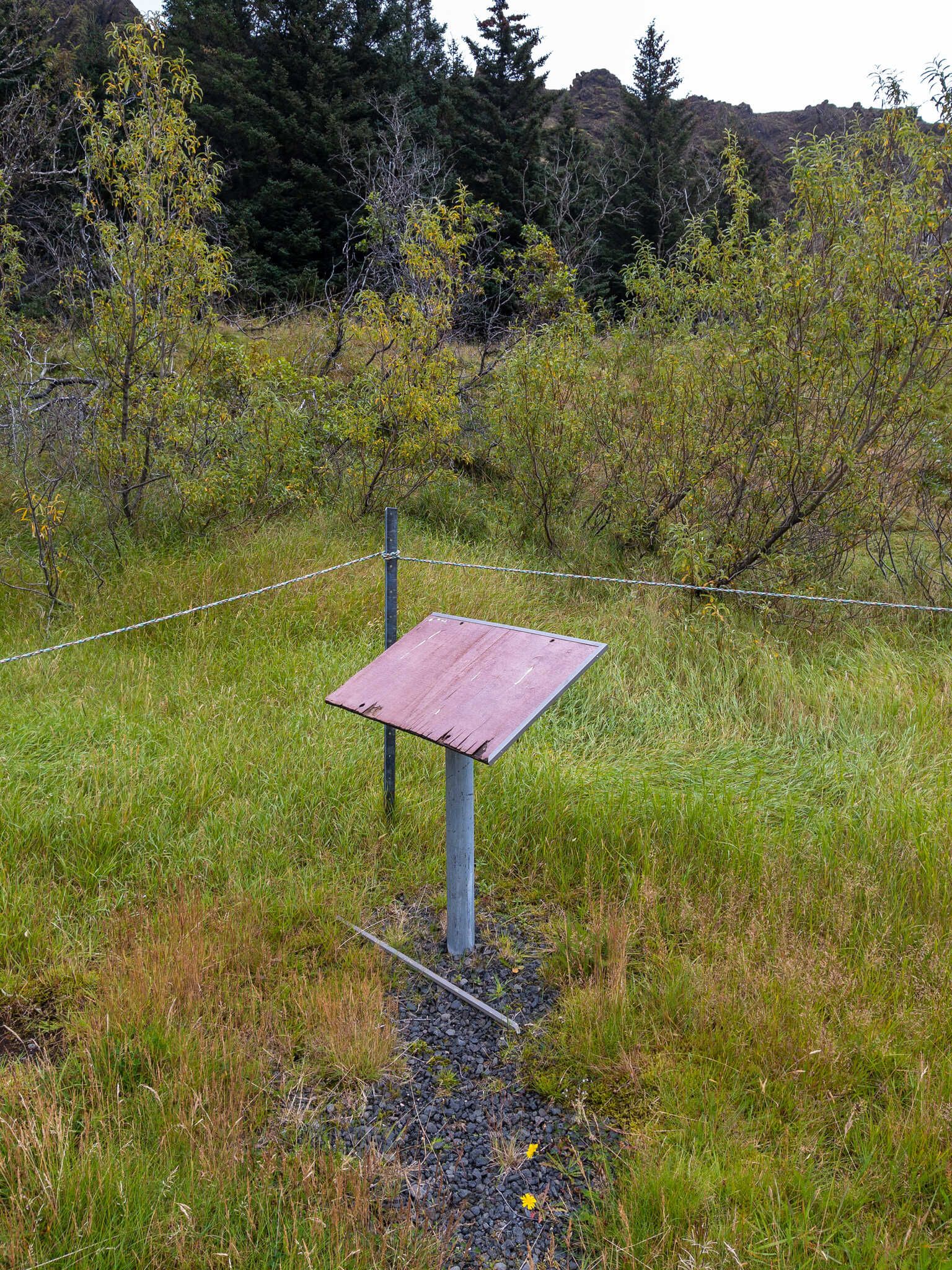 An old and worn sign that’s now blank, next to a simple wire barrier