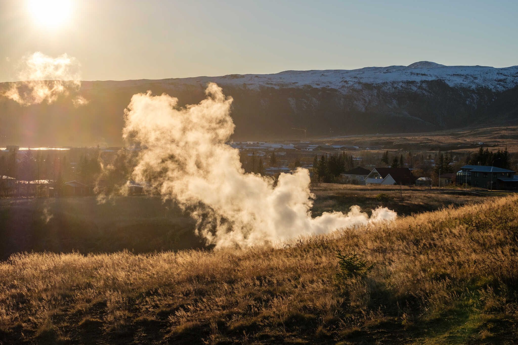 A plume of steam rises from a particularly active hot spring. The sun is setting off to the side of the picture