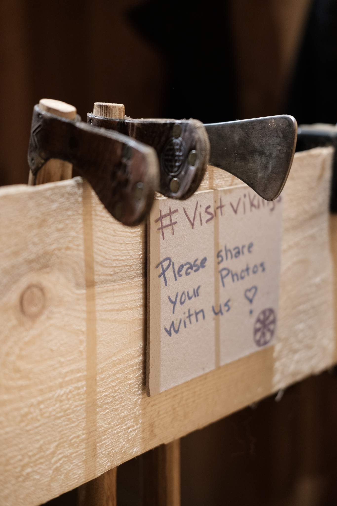 A row of viking axes hang on a plank. On the plank there is a sign that says: ‘#VisitVikings, Please share your photos with us.’ I did not.