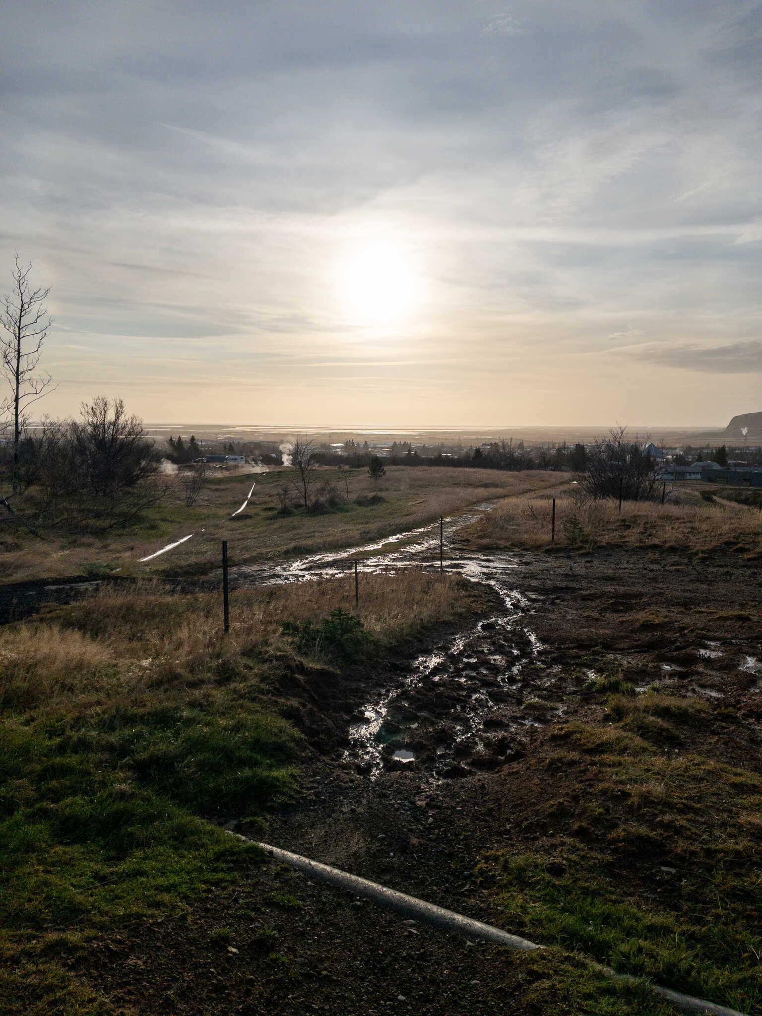 The sun is ahead of us, causing the water in a stream and the insulated pipes to shine