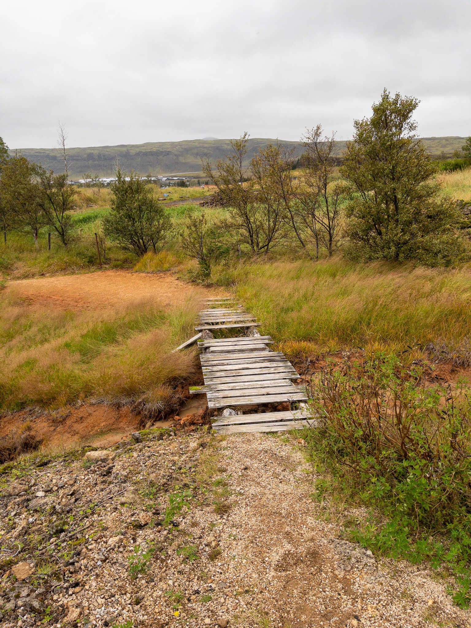 A very rickety “bridge” that is just a bunch of broken planks over a small geothermal stream