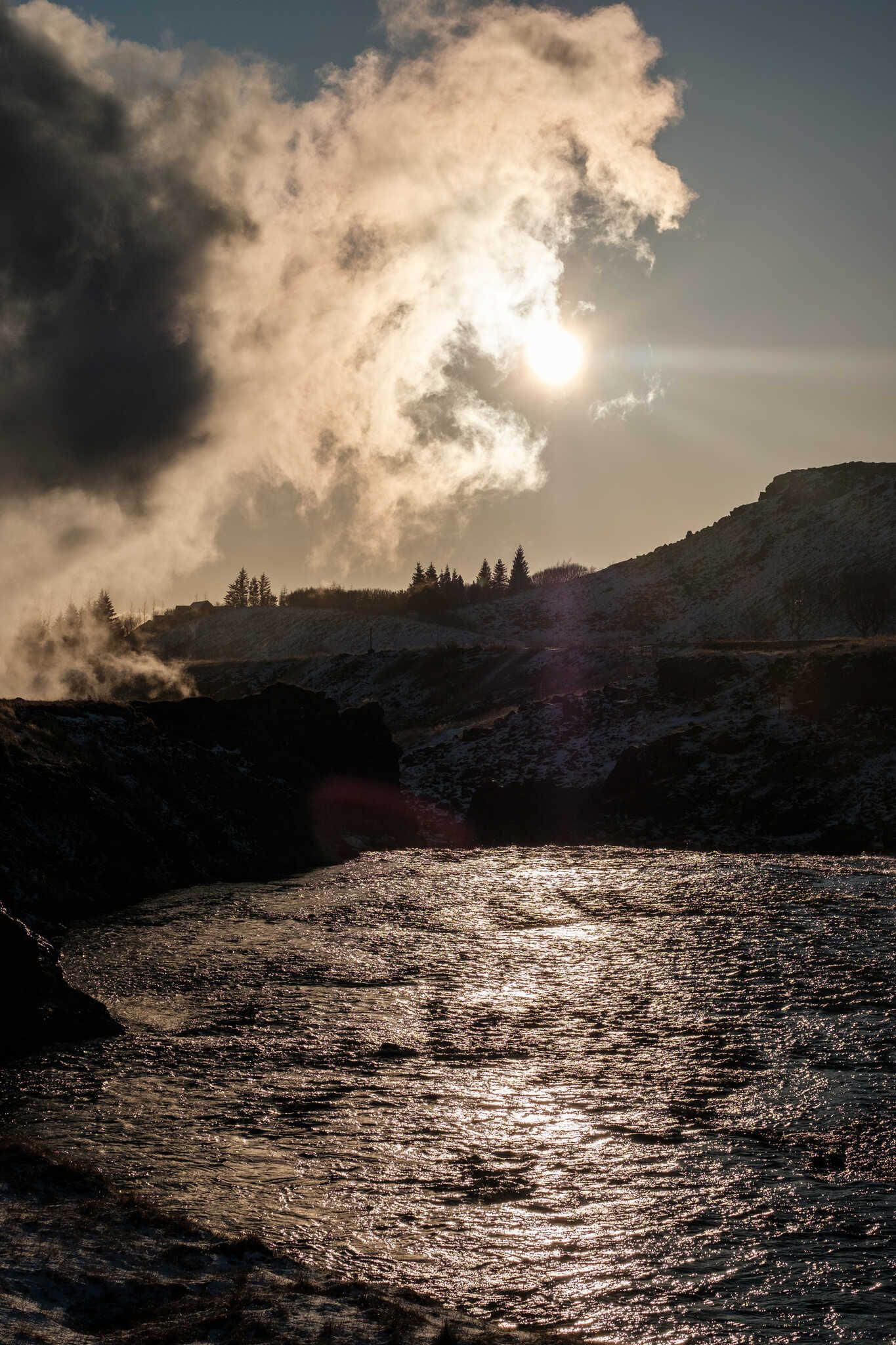 Steam flows over Varmá river. We can see trees on the other bank.