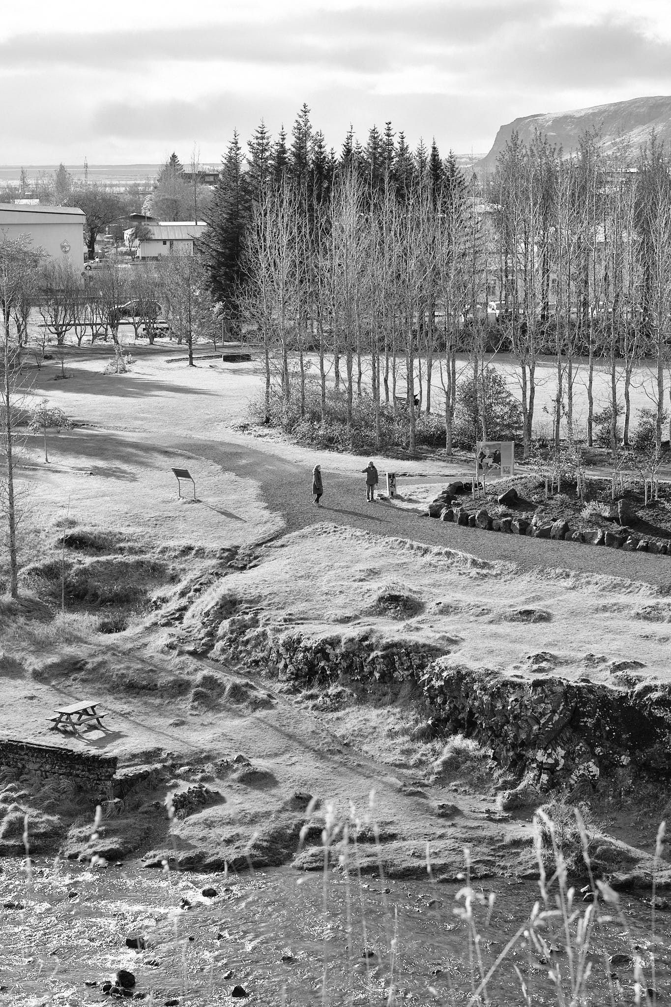 Two people walk in a park across the river