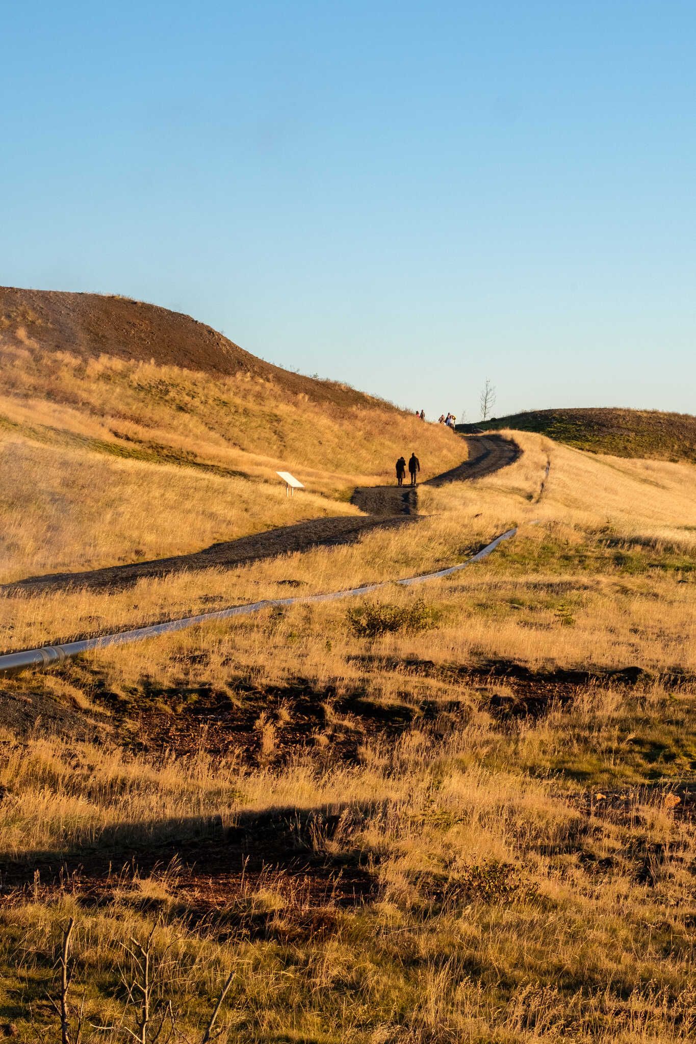 Two people walk the path ahead as it curves around a hill